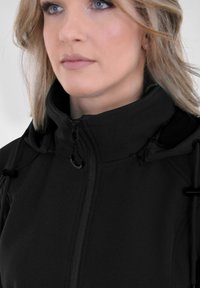 Zwarte zip-up jas met een hoge kraag, voorzien van trekkoordaccenten en een soepele stoftextuur. Close-up van het bovenlichaam.