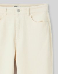 Pantalons en velours côtelé couleur crème avec une texture lisse, design à cinq poches et fermeture à bouton en métal à la taille. Motif à côtes verticales.