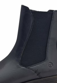 Bota de tobillo de cuero azul marino con un panel de malla texturizada, inserto elástico en los costados, costuras en contraste y un sutil detalle de logo en el lateral.