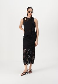 Musta ilmaõlaga top, millel on läbipaistev kate, koos musta pitsist midi seelikuga, millel on lillemuster ja laineline äär, täiendatud rihmadega kontsakingadega.