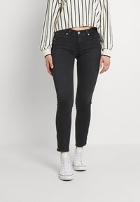 Jeans negros ajustados con una cintura de medio talle, con un detalle de cremallera en los tobillos y una textura de tela suave.