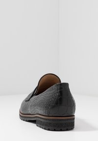 Mocassin en cuir noir à motif crocodile texturé, semelle en caoutchouc plate et petit talon. Doublure intérieure lisse.