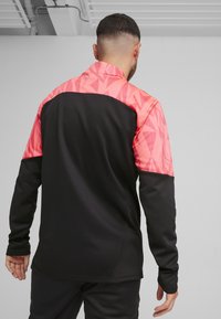 Schwarze und rosa Sportjacke mit geometrischem Muster auf dem oberen Rücken und den Ärmeln. Lange Ärmel und Kragen, mit einer glatten Textur.