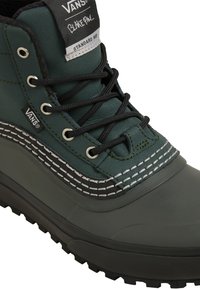 Stivale verde impermeabile a metà altezza con lacci neri, suola in gomma e cuciture bianche a contrasto. Presenta etichetta con marchio sulla linguetta e sul lato.