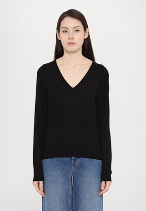 Maglione nero a V con maniche lunghe, realizzato in materiale morbido, abbinato a jeans a gamba larga azzurri, caratterizzati da un taglio rilassato e un design semplice.