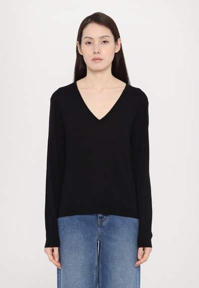 Schwarzer V-Ausschnitt-Pullover mit langen Ärmeln, aus weichem Material, kombiniert mit hellblauen, weit geschnittenen Jeans, die eine lockere Passform und ein schlichtes Design aufweisen.