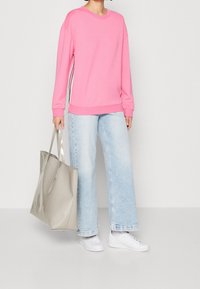 Sudadera rosa con cuello redondo, mangas largas y rayas laterales, combinada con vaqueros de pierna ancha de color azul claro y un bolso de mano beige. Zapatillas blancas.