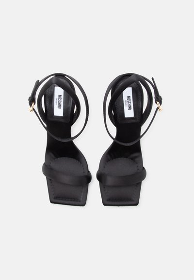 Μαύρα σανδάλια με τετράγωνη μύτη, λουράκια στον αστράγαλο και χρυσές αγκράφες, με το λογότυπο Moschino στην εσωτερική σόλα.