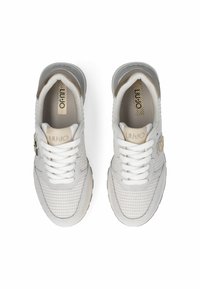 Zapatillas gris claro con parte superior de malla tejida, acentos beige en contraste, cordones blancos y suelas de goma texturizadas. Nombre de la marca visible en la lengua.