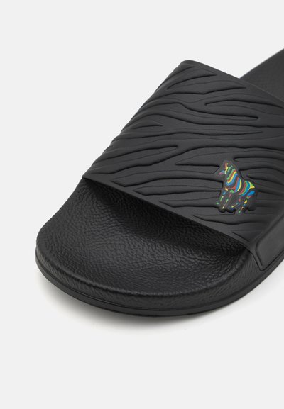 Black slide sandal with textured wavy pattern, rubber material, flat sole, and a multicolored zebra logo on the strap.