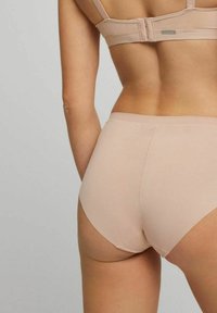 Ropa interior beis sin costuras con un diseño de altura media, que presenta una textura suave y bordes curvados para mayor comodidad y un ajuste aerodinámico.