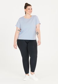 Ljusblå kortärmad t-shirt med rund halsringning, kombinerad med svarta högmidjade leggings och vita sneakers. Slät tygtextur.