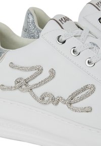 Baskets en cuir blanc avec un talon en paillettes argentées, logo "Karl" orné de strass et œillets en métal pour les lacets.