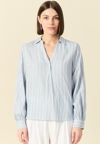 Blusa azzurra chiara a maniche lunghe con strisce bianche verticali, colletto e polsini arricciati. Tessuto morbido e liscio con una vestibilità rilassata.