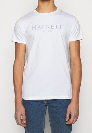 T-shirt en coton blanc avec un logo "HACKETT LONDON" bleu clair sur le devant. Col rond classique et manches courtes. Design simple.