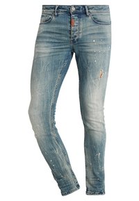 Vaqueros ajustados de color azul claro con detalles desgastados y rotos, que incluyen manchas de pintura y un pequeño desgarro en el muslo derecho.