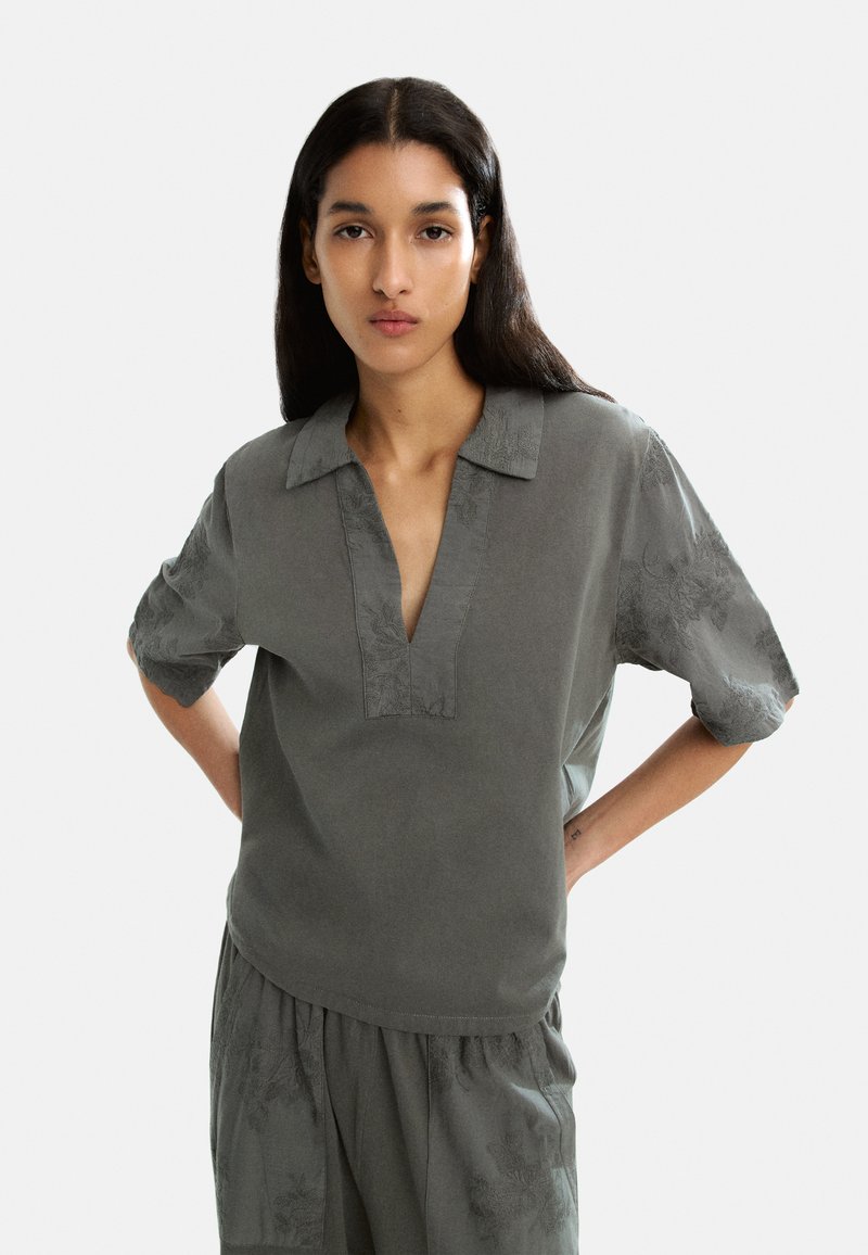 Top grigio a maniche corte con scollatura a V e dettagli floreali. Tessuto leggero con una vestibilità comoda, adatto per un abbigliamento casual.