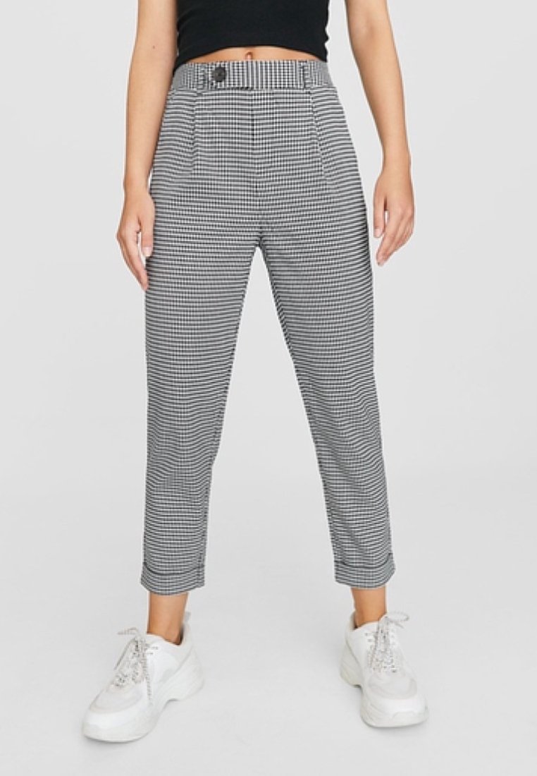 Femme portant un pantalon à carreaux noir et blanc taille haute et court, associé à des baskets blanches épaisses et un top court noir.