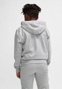 Grauer Hoodie mit verstellbarem Kapuzenzug, gerippten Bündchen und elastischem Saum. Der Stoff wirkt weich und leicht strukturiert. Kombiniert mit passenden Hosen.