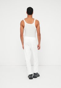 Λευκό αμάνικο τοπ και λευκή φόρμα που φοριούνται μαζί, με χαλαρή εφαρμογή, ελαστική μέση και λεπτομέρεια πίσω τσέπης. Μαύρα παπούτσια ολοκληρώνουν την εμφάνιση.