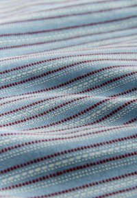 Tissu bleu clair avec un motif tricoté texturé comprenant de petites rayures horizontales blanches et fines rouge foncé.