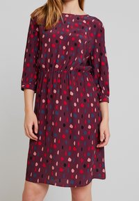 Vínová šaty se třičtvrtinovými rukávy a elastickým pasem. Vyznačují se vzorem červených, růžových, černých a modrých teček na hladkém materiálu.