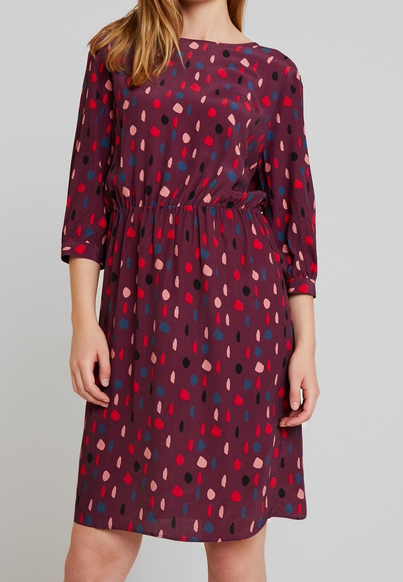 Vínová šaty se třičtvrtinovými rukávy a elastickým pasem. Vyznačují se vzorem červených, růžových, černých a modrých teček na hladkém materiálu.