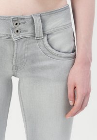 Fittet grå denim jeans med knap og lynlås, frontlomme og subtile falmningsdetaljer. Glat tekstur og tætsiddende ben.