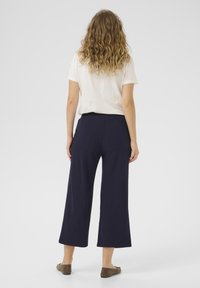 Pantaloni culotte blu navy con vestibilità comoda e vita elastica, abbinati a una maglietta di colore chiaro, visti da dietro.