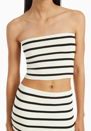 Vrouw draagt een witte geribbelde strapless cropped top en bijpassende rok met horizontale zwarte strepen.