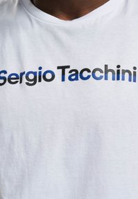 Hvit bomulls t-skjorte med teksten "Sergio Tacchini" i fet svart og blå gradientbokstaver. Rund hals, myk tekstur.