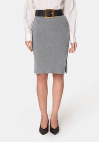 Grauer Strick-Bleistiftrock mit einem seitlichen Schlitz, kombiniert mit einem breiten schwarzen Gürtel mit einer goldenen quadratischen Schnalle. Dazu werden spitze schwarze High Heels getragen.