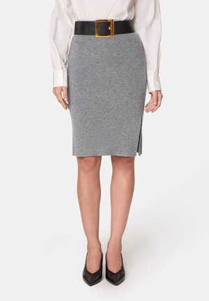 Jupe crayon en tricot gris avec une fente latérale, assortie d'une large ceinture noire avec une boucle carrée en or. Portée avec des escarpins noirs à bout pointu.