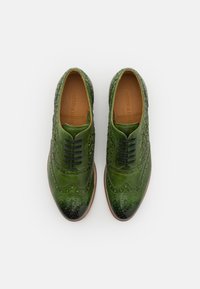 Zelené kožené brogue boty s propracovaným perforováním a hladkým povrchem. Mají černé tkaničky a světle hnědou podrážku.