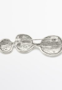 Silver-tone brooch with an abstract shape, featuring a textured surface and a pin fastening on the back, engraved with "Massimo Dutti."
