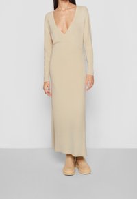 Robe en maille à manches longues de couleur beige clair avec un décolleté en V profond et un design portefeuille, complétée par des chaussures à plateforme beiges. Texture lisse.
