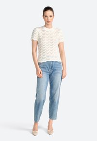 Hvid, tekstureret striktop med et bølgemønster, parret med lyseblå jeans og beige spidse hæle. Simpel, afslappet design.