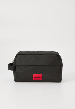 Black nylon toiletry bag with a top zipper, flat design, small handle, and a prominent red rectangular logo patch reading "HUGO."