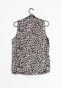 Blouse sans manches en tissu léger, avec un fond beige et un motif à pois noirs, présenté sur un cintre noir.