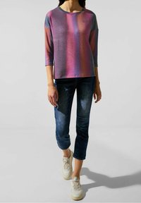 Pestrobarevný top s dlouhým rukávem se fialovými, růžovými a modrými pruhy, doplněný tmavě modrými zkrácenými džínami a bílými teniskami.