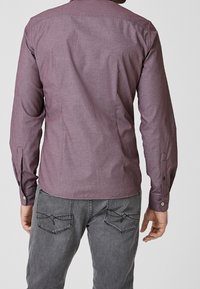 Mörkröd långärmad skjorta med ett texturerat mönster, med knäppärmar och en ryggsömn, matchad med grå denimbyxor med fickdetaljer.