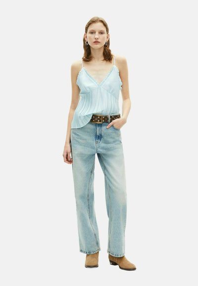 Top camisole a righe blu chiaro con bordi arricciati, abbinato a jeans blu chiaro a vita alta e stivali cowboy alla caviglia color tan. Cintura marrone con borchie.