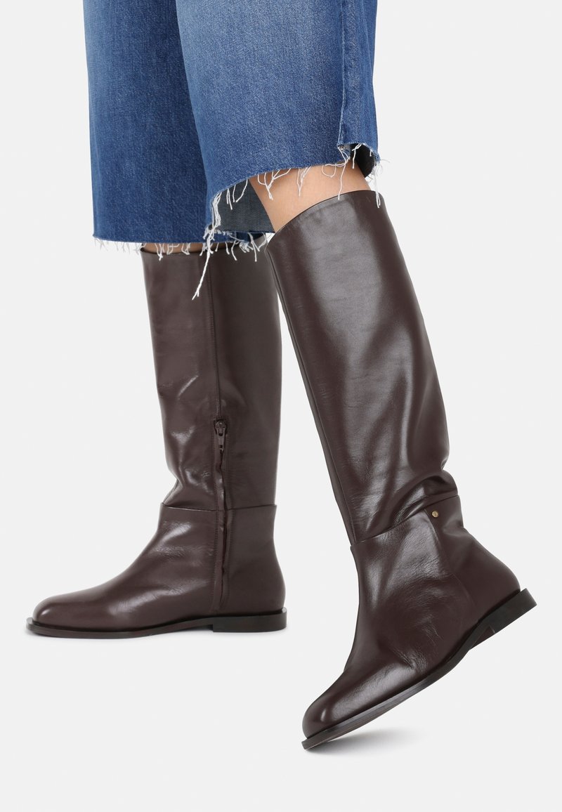 Brown leather knee-high boots with a smooth texture, side zipper, and flat soles. Ankle-width cuff with a small decorative accent.