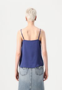 Camisola blu con spalline sottili, tessuto leggero e taglio rilassato, abbinata a una gonna di jeans chiara con tasche posteriori.