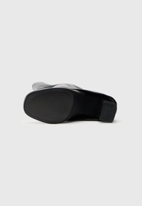 Black leather shoe with a rounded toe, low block heel, and textured rubber sole, displaying a smooth finish without visible embellishments.
