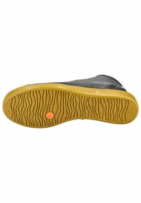 Zapato de cuero negro con una suela de goma texturizada, que presenta un patrón ondulado y un punto de acento naranja. La suela es amarilla con estrías para mayor tracción.