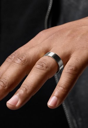 Metal ring with a polished silver finish, flat design, smooth texture, worn on a hand with natural fingernails, against a dark background.