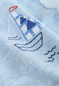 Tela azul claro con un diseño bordado de un velero, con una vela a cuadros azul y blanca, acentos rojos y líneas onduladas en azul marino.