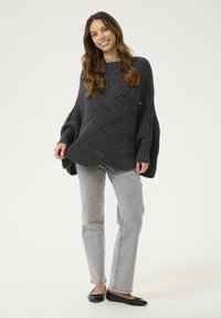 Jersey de punto grueso gris con un patrón de ondas, mangas acampanadas y un corte holgado, combinado con jeans rectos gris claro y bailarinas negras.