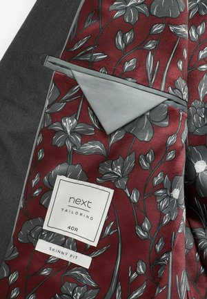 Interno di giacca su misura borgogna con motivo floreale grigio e una texture liscia. L'etichetta riporta "next Tailoring 40R Skinny Fit."
